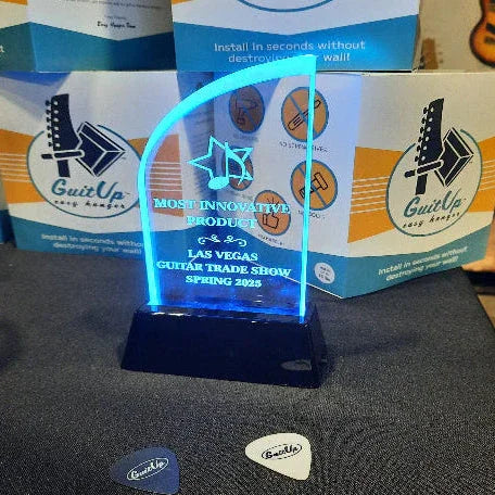 Blue acrylic award for most innovative guitar hanger, displayed with guitar picks and packaging box