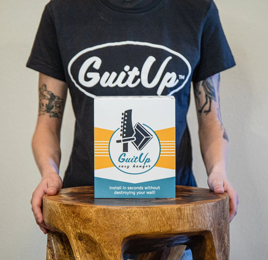 Person holding GuitUp Easy Hanger box for guitar wall mounting on wooden stool