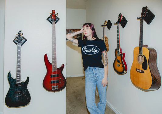 Person standing next to wall-mounted guitars and basses using easy hangers in a home setting
