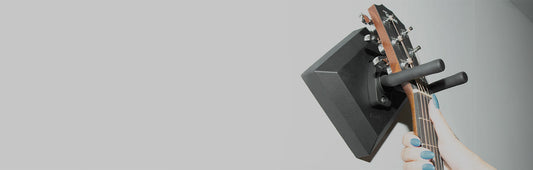 Hand placing acoustic guitar on a wall-mounted easy guitar hanger indoors