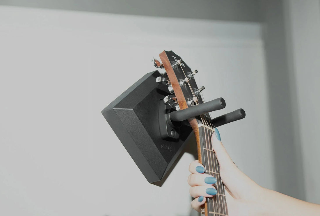 Hand hanging acoustic guitar on easy wall mount hanger indoors
