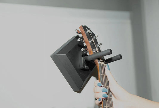 Hand hanging acoustic guitar on easy wall mount hanger indoors