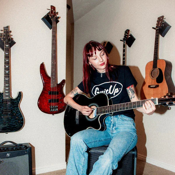 Woman playing acoustic guitar in room with multiple guitars wall-mounted using easy hangers