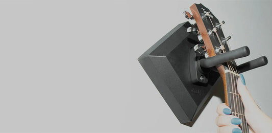 Hand hanging guitar on a black wall-mounted guitar hanger against a light background